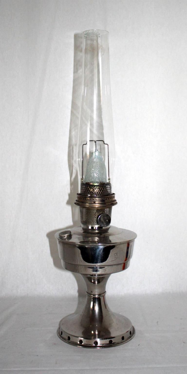 Eine glänzende Metalllampe mit hohem Glaszylinder auf rundem Standfuß